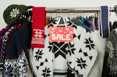 Close up on a big sale sign for winter clothes. Clearance rack with colorful winter outfits and accessories displayed on hangers.の写真素材