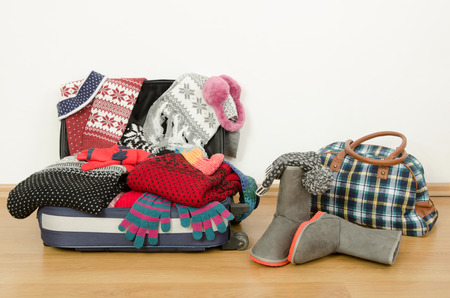 Winter luggage. Suitcase full of wither clothes. Packing the suitcase for Christmas vacation. Full luggage and bag with clothes and accessories.の写真素材