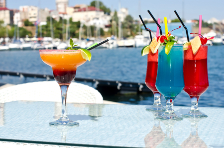 Summer colored fruit cocktail. Colorful exotic drinks served on the rocks with the seaside in the background.の写真素材