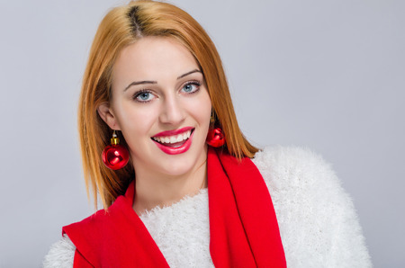 Beautiful young woman smiling with red balls earrings. Girl dressed for Christmas time. Merry Christmas.の写真素材