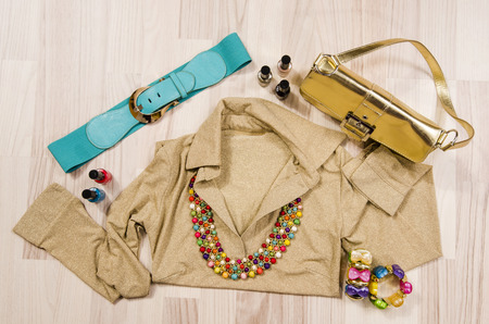 Gold blouse and accessories arranged on the floor. Woman gold and colorful accessories, blue belt. necklace, bracelets and nail polish.の写真素材