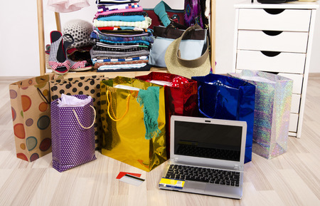 Wardrobe with clothes and shopping bags, on line shopping. Close up on a laptop and credit cards, internet buying for Christmas, many full bags in a woman closet.の写真素材