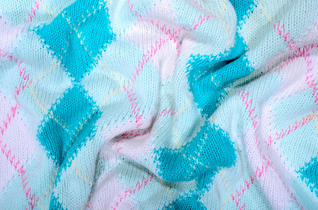 Close up on crumpled knit woolen  fabric  texture. Blue rhombus woven sweater as a background.