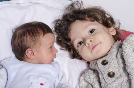 Portrait of a cute baby boy looking at his big brother. Newborn lying in bed bonding with his...