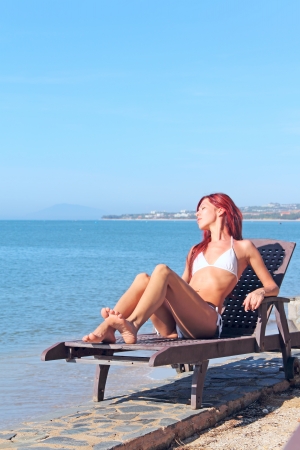 Young woman sitting on chaise lounge at the beachの写真素材