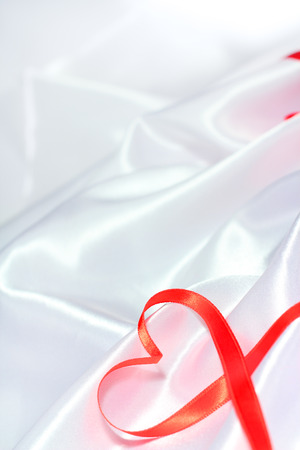 Red satin glossy ribbon heart over white silk backgroundの写真素材