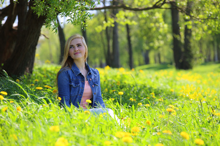 Beautiful young woman sitting in spring park with dandelion flowersの写真素材