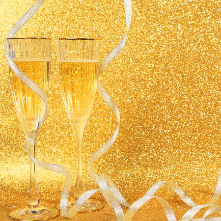 Two glasses of champagne with golden glitter lights on backgroundの写真素材