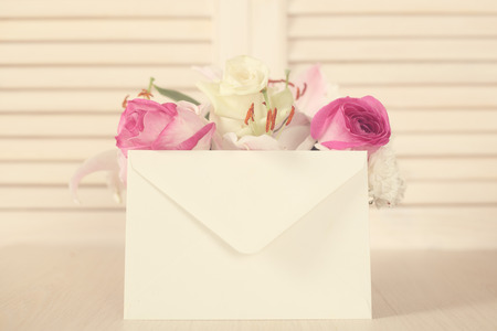 Basket of flowers and blank envelope on wooden background