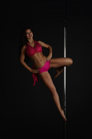 Beautiful woman performing pole dance on dark backgroundの写真素材