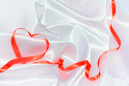 Red satin glossy ribbon heart over white silk backgroundの写真素材