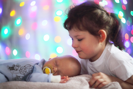 Newborn baby and his sister on glowing bokeh lights background