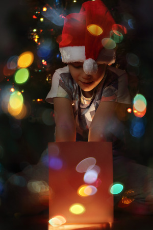 Happy little boy opens his magic glowing christmas gift near decorated christmas treeの写真素材