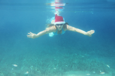 Woman in Santa Claus hat swimming underwater in sea, Christmas vacation at sea concept