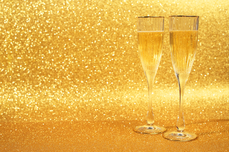 Two glasses of champagne with golden glitter lights on backgroundの写真素材