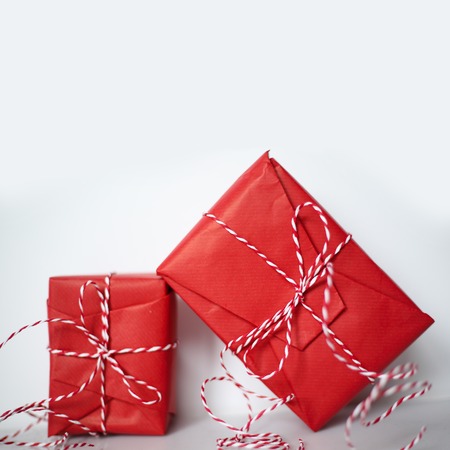 Christmas gift boxes wrapped in red paper and bow of dtriped rope on white background