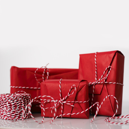 Christmas gift boxes wrapped in red paper and bow of dtriped rope on white backgroundの写真素材