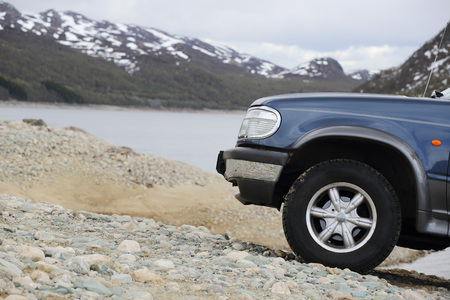 Big SUV car wheel stands on backdrop of mountain lake