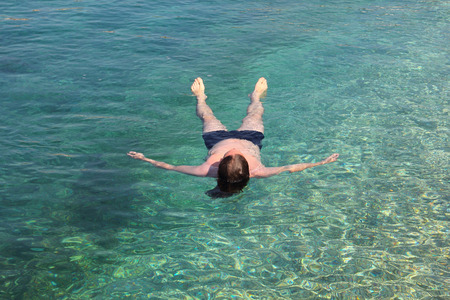 Vacation and relaxation concept, man floating relaxed on back in transparent pure blue sea waterの写真素材
