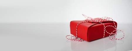 Christmas gift box wrapped in red paper and bow of dtriped rope on white backgroundの写真素材