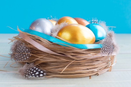 Beautiful Happy Easter holiday greeting banner with easter nest with colored eggs and decorated with ribbons over light wooden background with copy space for text on blueの写真素材