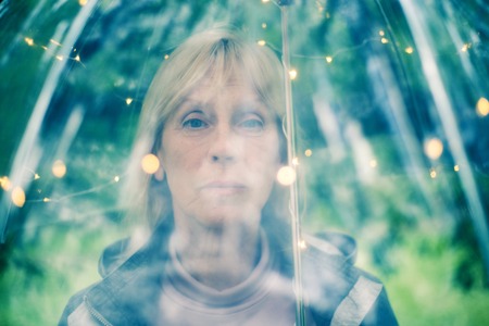 Portrait of beautiful senior woman with transparent umbrella with light bokeh background