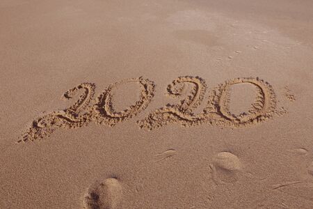 Happy New Year 2020, lettering on the beach. Numbers 2020 year on the sea shore, message handwritten in the golden sand on beautiful beach background. New Years concept.の写真素材