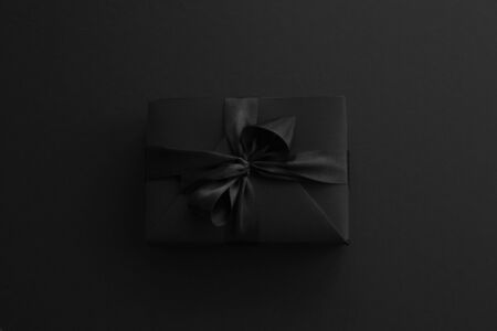 Black friday gift, paper box with silk ribbon bow on black paper background with copy space for text, flat lay top view templateの写真素材