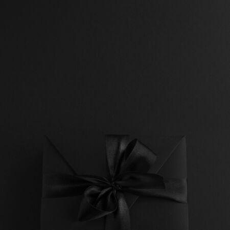 Black friday gift, paper box with silk ribbon bow on black paper background with copy space for text, flat lay top view templateの写真素材