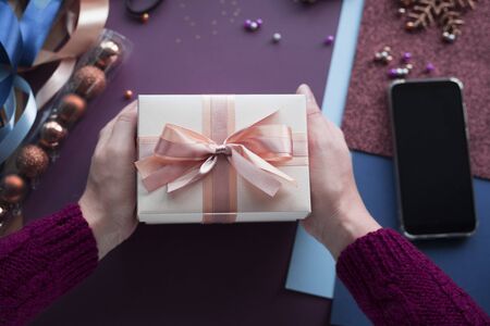 Female hands holding present gift for Christmas. Top view at workplace for preparing handmade...