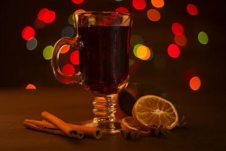 Mulled wine with cinnamon sticks and orange over holiday christmas lights backgroundの写真素材