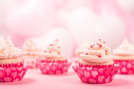 Valentine day love cupcakes decorated with cream and hearts on pink and white party balloons background with copy space for textの写真素材