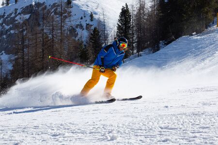 Male skier in blue and yellow clothes on slope with mountains in the background at Cortina d'Ampezzo Faloria skiing resort area Dolomiti Italyの写真素材