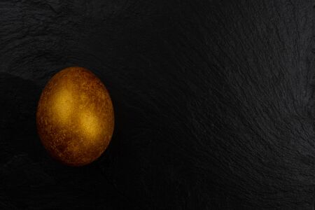 One big golden easter egg on dark black stone background copy space for textの写真素材
