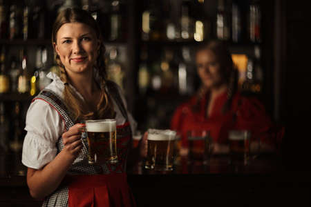Pretty oktoberfest blonde woman holding beer mugs in barの写真素材
