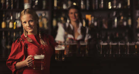 Pretty oktoberfest blonde woman holding beer mugs in barの写真素材