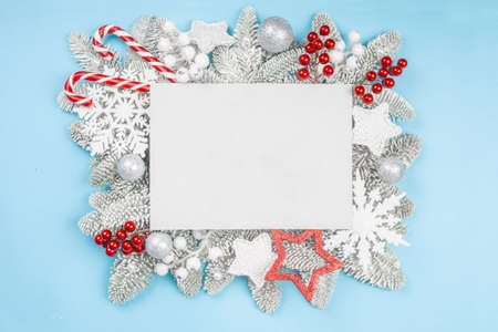 Frosted fir tree twigs and Christmas decorative bauble balls on blue background with white rectangle...