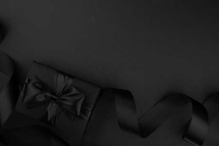 Black friday gift, paper box with silk ribbon bow on black paper background with copy space for text, flat lay top view templateの写真素材