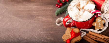 Cocoa in red mug with marshmallows candy cane fir tree branches and red baubles on dark wooden background with bokeh lightsの写真素材
