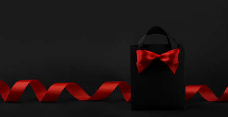 Gift in black paper bag with red ribbon on black background, design banner black friday sale concept copy space for textの写真素材