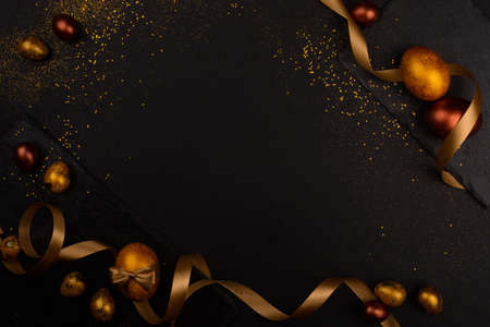 Golden luxury easter eggs and ribbon composition boder frame on black stone background with copy...