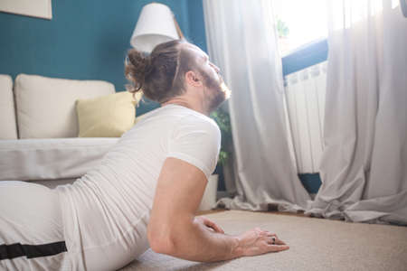 Mid adult mature man in white sport clothes practice yoga stretch doing exercise at home...