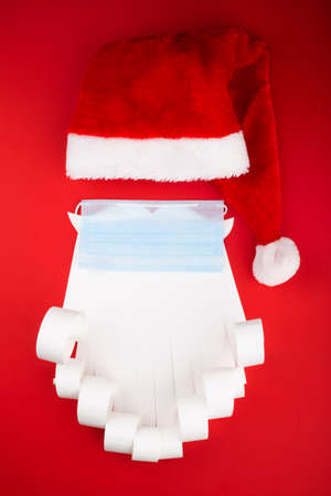 Santa Claus beard hat with face mask on red background, creative minimal concept of Christmas and New Year safe celebrationの写真素材