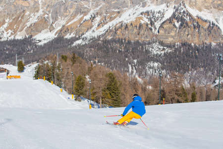 Male skier in blue and yellow clothes on slope with mountains in the background at Cortina d'Ampezzo Faloria skiing resort area Dolomiti Italyの写真素材