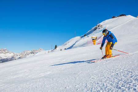 Male skier in blue and yellow clothes on slope with mountains in the background at Cortina d'Ampezzo Faloria skiing resort area Dolomiti Italyの写真素材