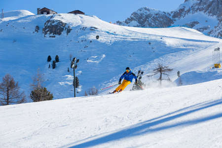 Male skier in blue and yellow clothes on slope with mountains in the background at Cortina d'Ampezzo Faloria skiing resort area Dolomiti Italyの写真素材