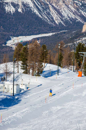 Male skier in blue and yellow clothes on slope with mountains in the background at Cortina d'Ampezzo Faloria skiing resort area Dolomiti Italyの写真素材