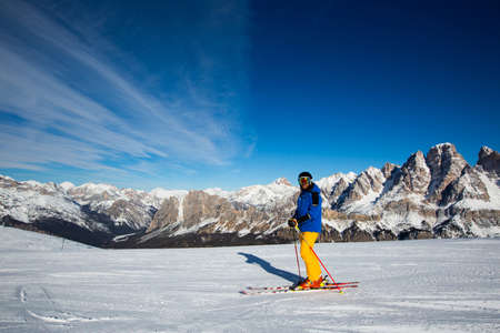 Male skier in blue and yellow clothes on slope with mountains in the background at Cortina d'Ampezzo Faloria skiing resort area Dolomiti Italyの写真素材