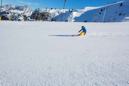 Male skier in blue and yellow clothes on slope with mountains in the background at Cortina d'Ampezzo Faloria skiing resort area Dolomiti Italyの写真素材