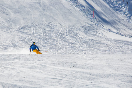 Male skier in blue and yellow clothes on slope with mountains in the background at Cortina d'Ampezzo Faloria skiing resort area Dolomiti Italyの写真素材